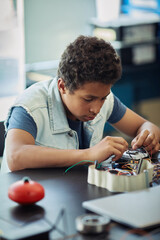 Wall Mural - Vertical portrait of black teenage boy building robot and wiring circuit panel during engineering class at school