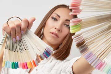 Wall Mural - Beautiful young serious woman looking at camera holdin nail tips. Beauty portrait of brunette girl