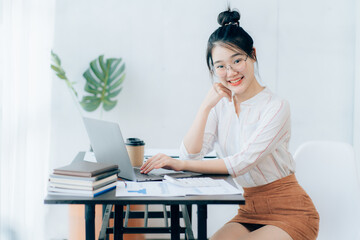 Portraits of beautiful smiling Asian women relax using laptop computer technology while sitting on their desks and using their creativity to work