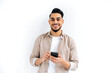 © Kateryna - Handsome positive Arabian or Indian modern guy, holding smartphone in his hands, messaging, looking excitedly at the camera, standing over isolated white background, smiling