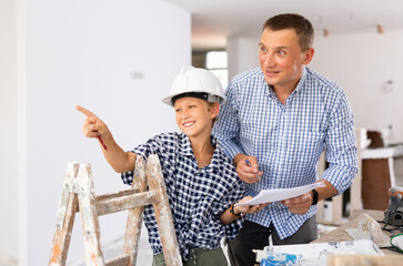 Wall Mural - Adult man and preteen boy holding documents and talking in new house, planning design projects