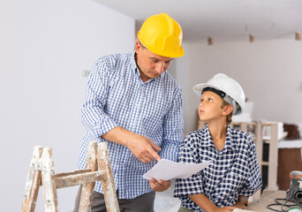 Wall Mural - Father and his young son wearing protective hardhats discussing work plan in construction site in apartment.