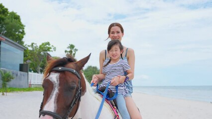 Wall Mural - Asian young mother and daughter horseback riding on the beach together