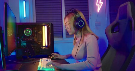 Canvas Print - Asian professional gamer playing online video game on desktop computer PC have colorful neon LED lights, young woman in gaming headphones using computer for playing game at home