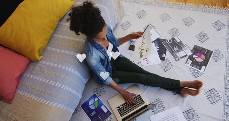 Canvas Print - Animation of white heart icons floating over african american woman reading documents on bed at home