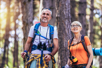 Senior couple hiking in forest wearing backpacks and hiking poles. Nordic walking, trekking. Healthy lifestyle.