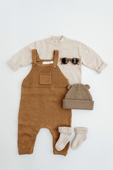 Wall Mural - Cute gender neutral baby clothes. Knitted jumpsuit, sweater, kids sunglasses, socks, warm hat. Stylish elegant neutral pastel colours newborn baby clothes, accessories. Flat lay, top view