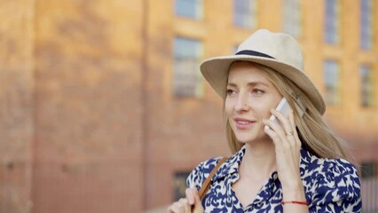 Wall Mural - Mid adult woman walking in summer in town and calling on mobile phone.