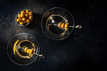 Martini, two glasses with spicy olives. Alcoholic cold drinks, shot from above on a black background with copy space, a flat lay