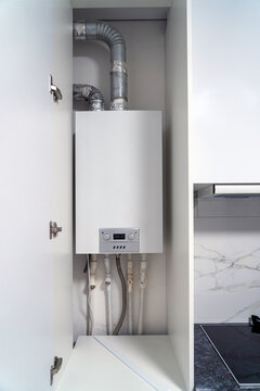 Opened kitchen cabinet and LPG gas boiler inside furniture. Gas central heating condensing boiler fitted inside cabinet.