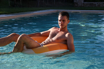 handsome young man  floating in a swimming pool looking in camera