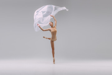 Wall Mural - Portrait of young beautiful ballerina dancing with transparent fabric isolated over grey studio background. Grace