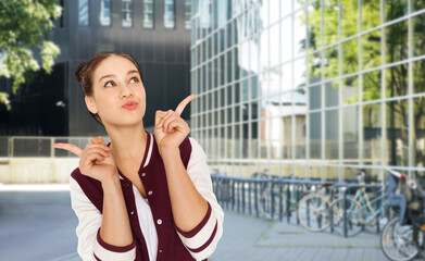 Poster - people, gesture and education concept - happy pretty teenage girl pointing fingers up over city street or school yard background