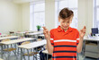 © Syda Productions - school, education and people concept - scared student boy in red polo t-shirt holding fingers crossed over empty classroom background