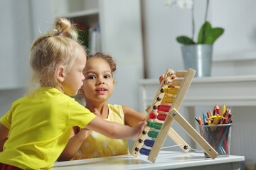 children of different races sit together at the table and count on the abacus