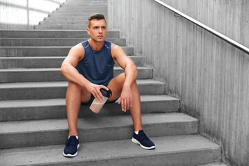 Wall Mural - fitness, sport and people concept - tired young man with protein shake in bottle sitting on stairs