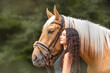 Portrait of a female equestrian beneath her palomino kinsky warmblood horse in summer outdoors