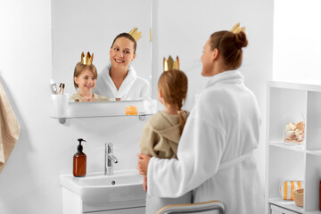 Sticker - beauty, family and people concept - happy smiling mother and daughter in crowns looking to mirror in bathroom