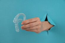 A Female Hand Sticking Out Of A Hole From A Blue Background Holds Removable Night Retainers. 