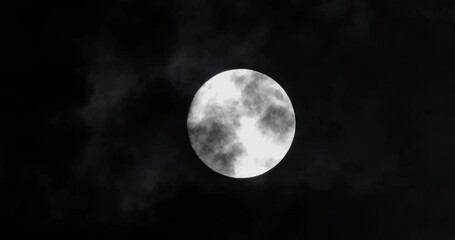 Wall Mural - Full moon at night. The illuminated face of the moon is wrapped in a cloud cover that covers it in a veiled way.