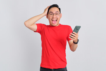 Wall Mural - Shocked young Asian man holding mobile phone and touching head with hand isolated over white background