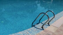 Stainless Steel Handrails For The Pool Against The Backdrop Of A Clean Pool With Blue Water. Handrails To Help Lower The Pool Into The Water. The Concept Of Accessibility Of Recreational Activities.