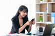 © amnaj - Beautiful Asian businesswoman using smartphone to check work contact customers, answer chats, complete transactions and use social media applications various in the office.