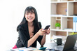 © amnaj - Beautiful Asian businesswoman using smartphone to check work contact customers, answer chats, complete transactions and use social media applications various in the office.