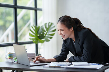 Wall Mural - Beautiful Asian businesswoman hurriedly checks at his desk with his laptop computer to check urgent document.