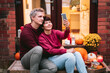 Couple taking selfies on phone during a romantic date on the porch of their home. Time at home. Autumn tea time outdoors on house entrance decorated with pumpkins, flowers and burning candles