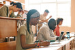 © AnnaStills - Group of students sitting at desk with laptop and books and writing exam at university