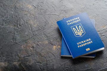 On a dark gray background are two Ukrainian biometric passports. Minimalism. Travel, business, emigration, Russia's war against Ukraine, refugees.