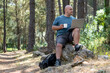 © MiguelAngel - Digital nomad man enjoys working with a laptop sitting on a rock in a forest.