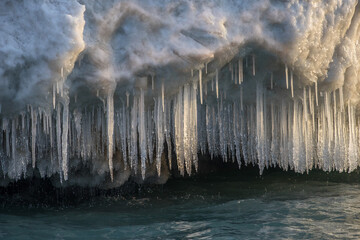 Icicles and snow dripping over water in sunlight