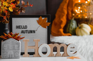 Cozy autumn concept. Home warmth in cold weather. Still-life. A blanket, pumpkins, flowers and the inscription home on the coffee table in the home interior of the living room.