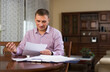 © JackF - Portrait of adult man working with papers and reading mail in cozy home interior..