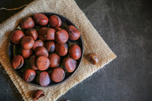 Chestnuts In Black Bowl Over Grey Background. Pile Of Fresh Chestnuts Ready To Roast. Top View, Copy Space.