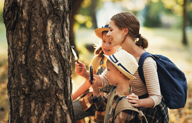 Нарру mother and two   children in   with backpacks examining tree bark through magnifying glass in forest