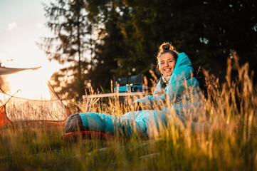 Wall Mural - Woman relaxing and lie in a sleeping bag in the tent. Sunset camping in forest. Mountains landscape travel lifestyle camping. Summer travel outdoor adventure