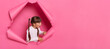 © sementsova321 - Portrait of amazed surprised little girl wearing striped shirt posing in pink paper torn, looking aside with open mouth and big eyes, copy space for advertisement or promotional text.