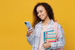 Young happy black teen girl student she wear casual clothes backpack bag hold books hold in hand use mobile cell phone isolated on plain yellow color background. High school university college concept