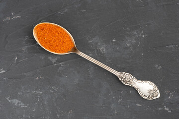 Wall Mural - Red chili pepper spice metal spoon on black concrete background. Macro. Top view. Healthy eating concept