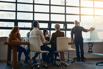 Mature leader talking to a group of businesspeople about a vision while planning an innovation project together as a team in a collaboration meeting. Smart male in discussion about a strategy idea