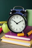 Fototapeta Tematy - Alarm clock and different stationery on wooden table near green chalkboard. School time