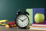 Fototapeta Tematy - Alarm clock and different stationery on wooden table near green chalkboard. School time