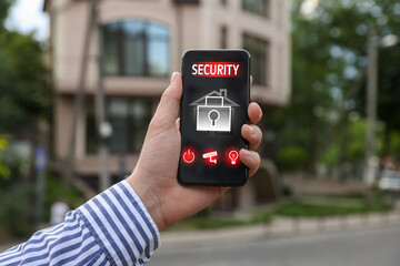 Man using home security application on smartphone in front of house outdoors, closeup