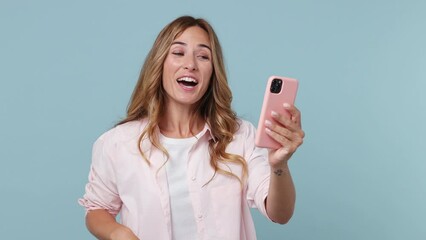 Wall Mural - Young fun woman 30s wear pink shirt get video call using mobile cell phone doing selfie talk conducting pleasant conversation greet with hand isolated on plain pastel light blue cyan background studio