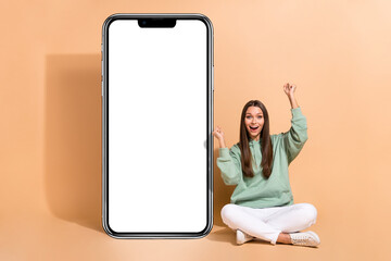 Portrait of attractive cheerful lucky girl sitting rejoicing new offer copy space isolated over beige pastel color background