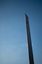 A Tall Rectangular Sharp Concrete Stele Against A Background Of Clear Blue And Blue Sky In The Shadow Of The Sun With The Russian Flag On Top
