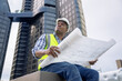© Basicdog - African male civil engineer inspects a commercial building construction site in a real estate project.